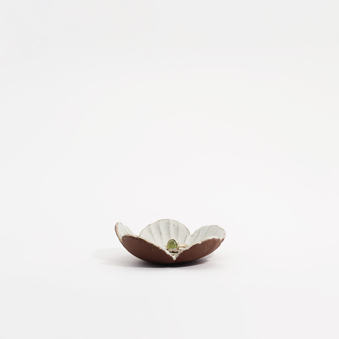 lille blomsterskål med en hvid glasur, der holder en gylden ring med en grøn ædelsten