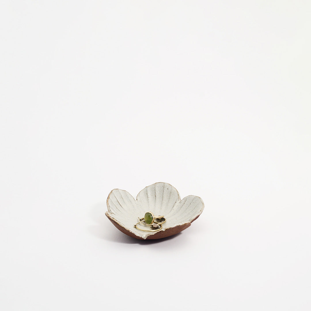 lille blomsterskål med en hvid glasur, der holder en gylden ring med en grøn ædelsten