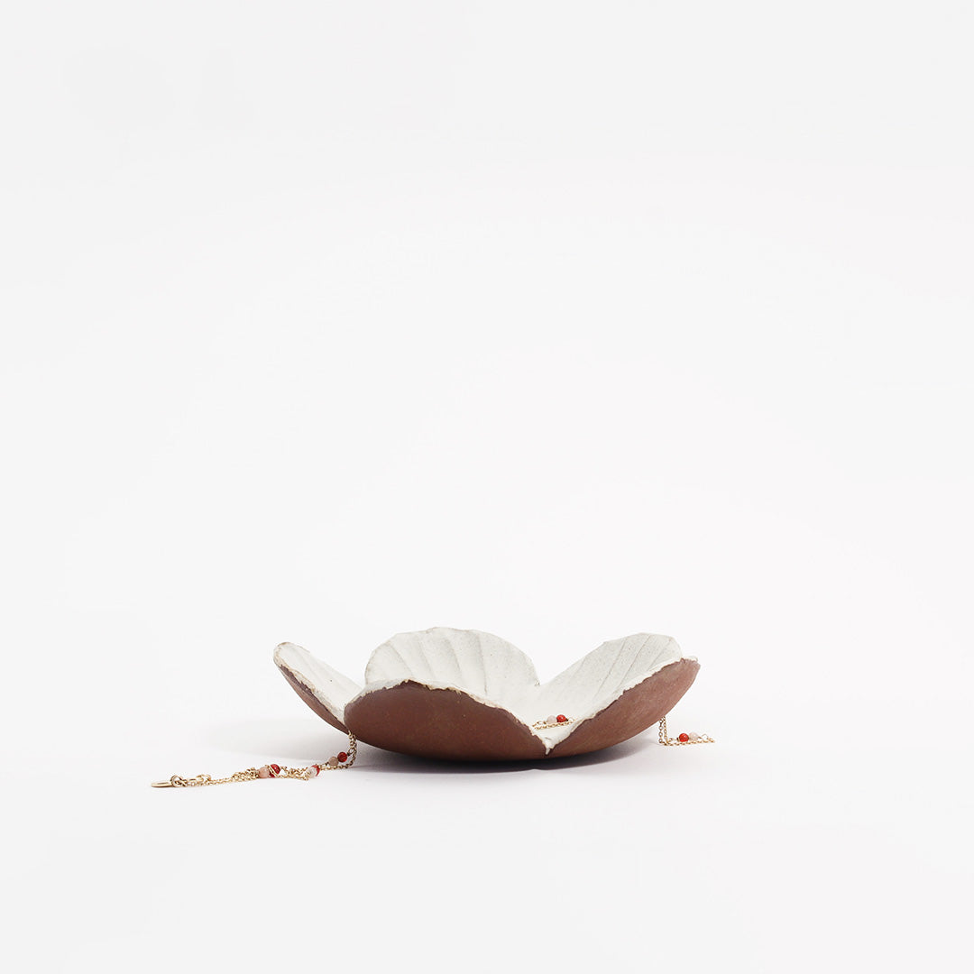 Blomsterskål, der holder en gylden halskæde, som ligger hen over skålen med en hvid glasur kaldet musling